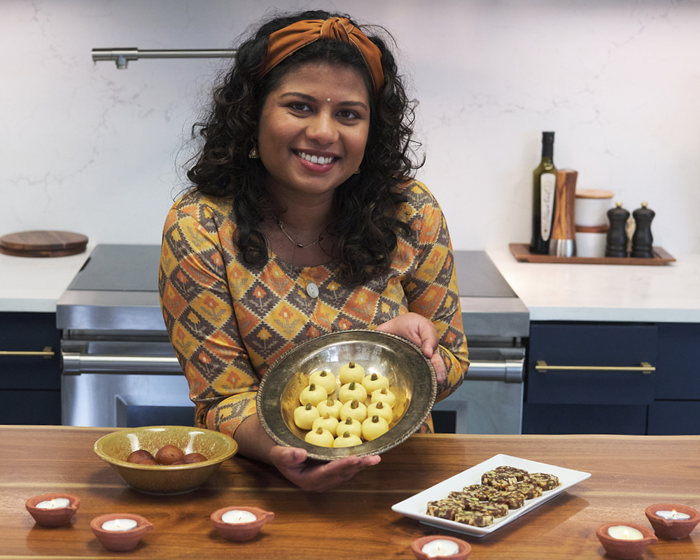 Shri Repp posing with three Diwali desserts in a kitchen