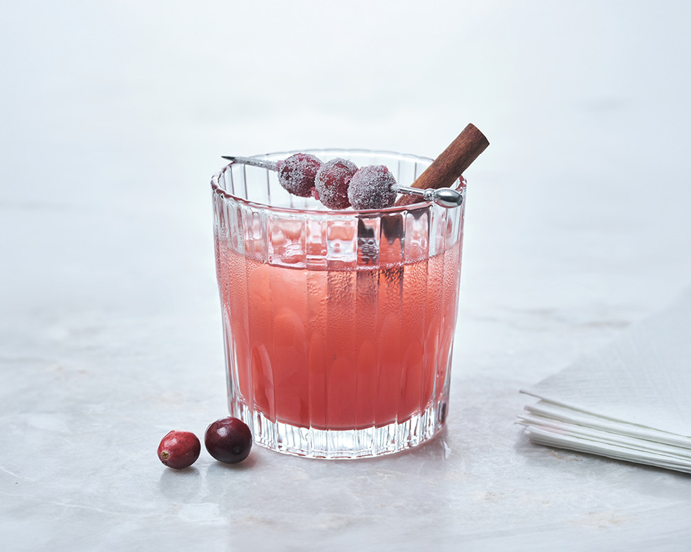 Winter Margarita Cocktail with sugared cranberries and a cinnamon stick on a white gray background