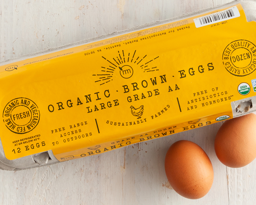 Metropolitan Market yellow egg carton with two eggs on a white wood table