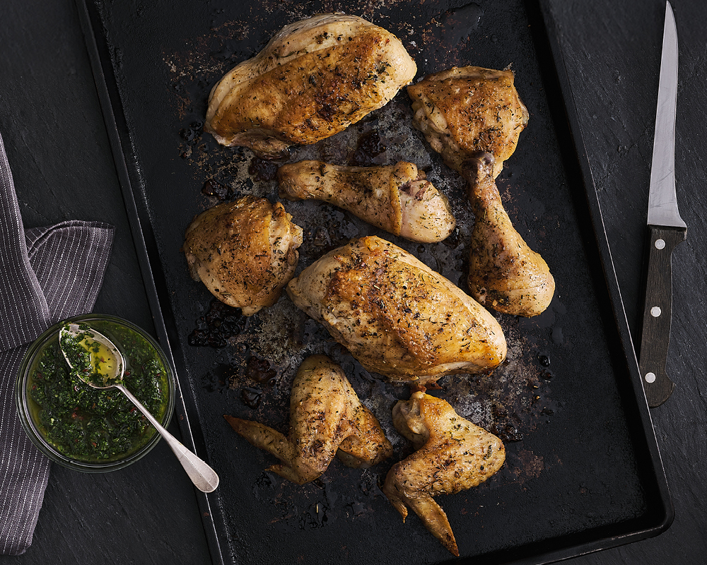 Deconstructed whole chicken on a pan with chimichurri sauce