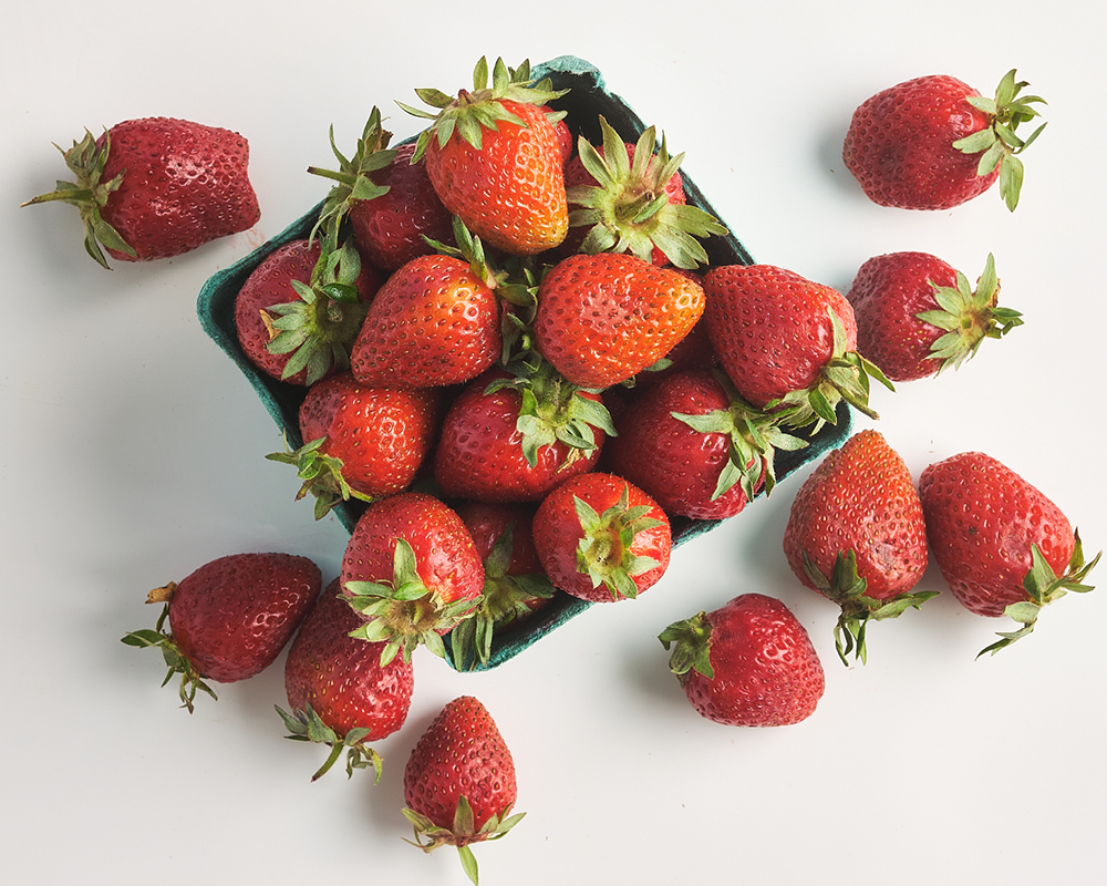 Spooner Farms strawberries in pint and scattered on white background