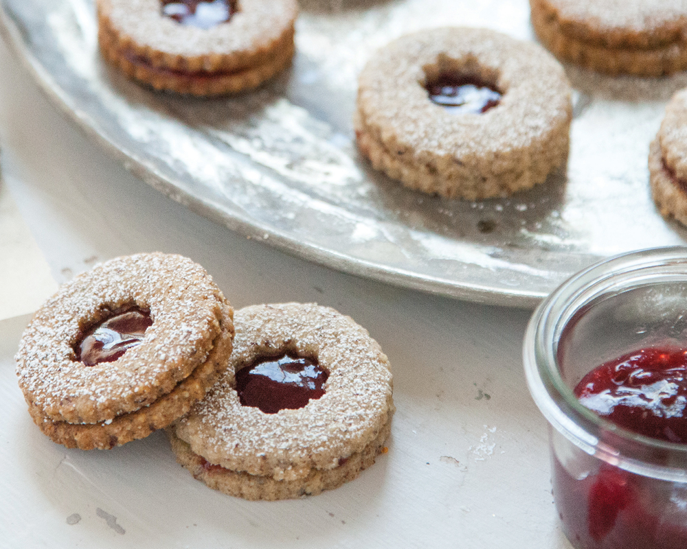 Linzer cookies on a marble countertop with a silver serving tray and bowl of red jam