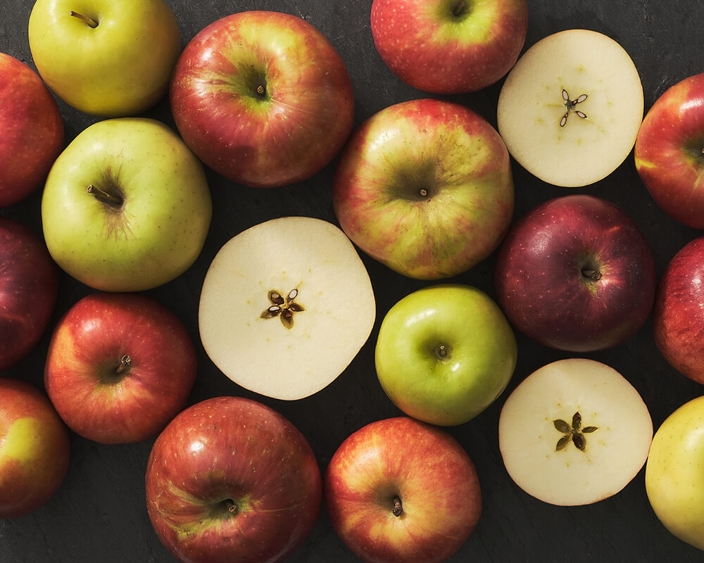 A group of red and green apples with some halved on a black background