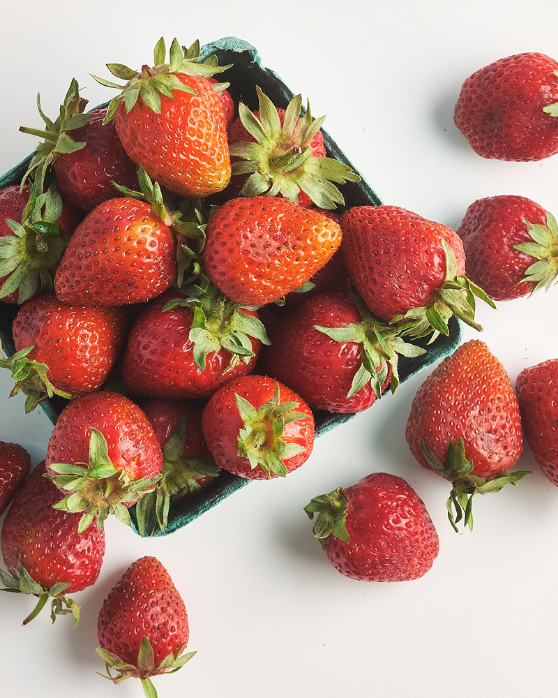 Spooner Farms strawberries in a pint and scattered on white background