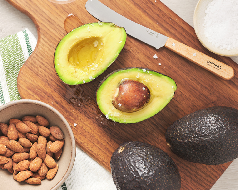 Halved avocados drizzled with oil and styled with whole avocados and almonds