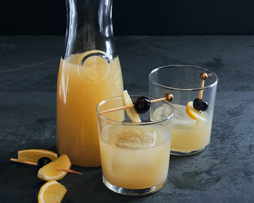 Whiskey sour in a pitcher and two glasses on a dark gray background